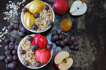 Fototapeta na wymiar Oatmeal in bowls with apples, pears and grapes. Healthy breakfast with oatmeal and fruit.