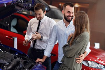 Fototapeta na wymiar Confident young salesman explaining car features to the young attractive owners