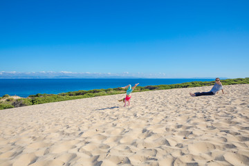Fototapeta na wymiar little girl doing handstand on sand next to mother