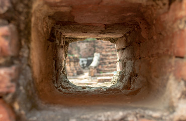 Blurred view through focused loophole in brick wall with ancient masonry on Wat Mahatha temple in Ayutthaya, Thailand. Light at the end of tunnel.