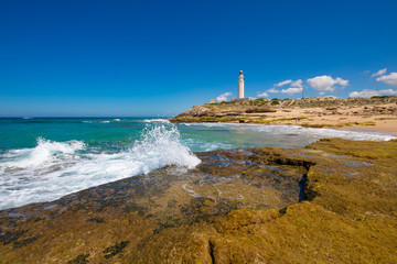 ocean wave breaking on coast rock next to Trafalgar lighthouse