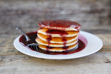 Stack of Pancakes with Blueberry Syrup on a Plate Outside on a Wood Table