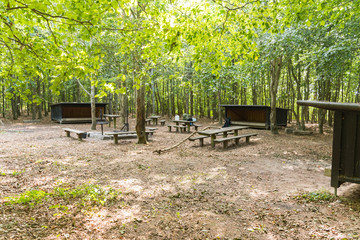 Three shelters in a green wood with fireplace and wooden tables - 231739035