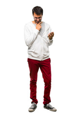 A full-length shot of a Man with glasses and listening music standing and looking down with the hand on the chin on white background