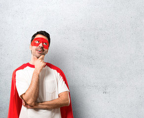 Superhero man with mask and red cape standing and thinking an idea on textured grey background