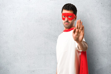 Superhero man with mask and red cape making stop gesture with her hand denying a situation that thinks wrong on textured grey background © luismolinero