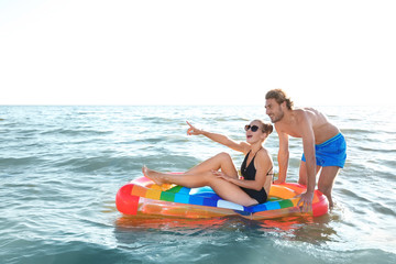 Happy young couple in beachwear swimming with inflatable mattress in sea