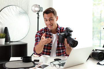 Portrait of photo blogger with camera and laptop at home. Online broadcast