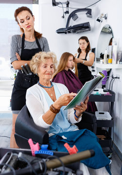 Young woman hairdresser in hair salon helping to senior woman ch