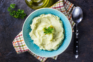 Mashed cauliflower with oil in blue bowl on wooden table.
