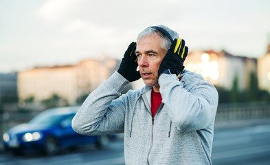 Mature male runner putting on headphones outdoors in city.