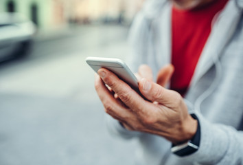 A close-up of unrecognizable man standing outdoors in city, using smartphone.