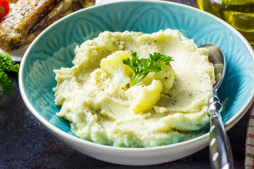 Mashed cauliflower with oil in blue bowl on wooden table.