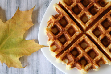 Belgian waffles and autumn maple leaf on wooden table. Fresh homemade breakfast