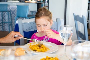 little girl eating paella from dish with angry expression