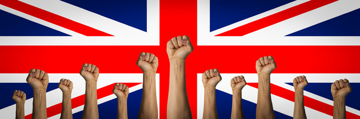 Hands raised up and clenched in a fist against the background of the United Kingdom flag. Concept of unity of the people of Great Britain, revolution, revival, riot. Banner