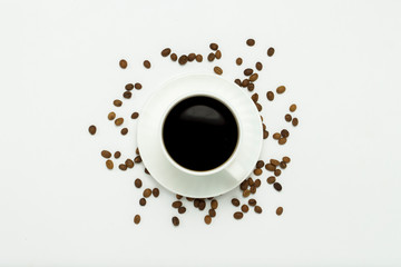A white cup with a saucer and black coffee, coffee grains are scattered around on a white background. Flat lay, top view