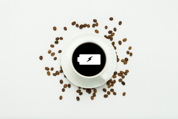 White cup with a saucer and black coffee and a battery icon, coffee grains are scattered around on a white background. Concept of charging energy for the whole day. Flat lay, top view