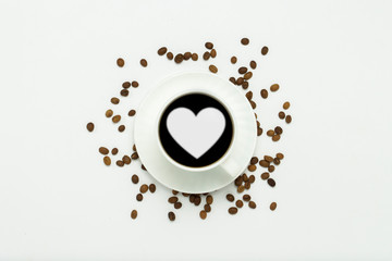 white cup with a saucer and black coffee and a heart icon, coffee grains are scattered around on a white background. Flat lay, top view