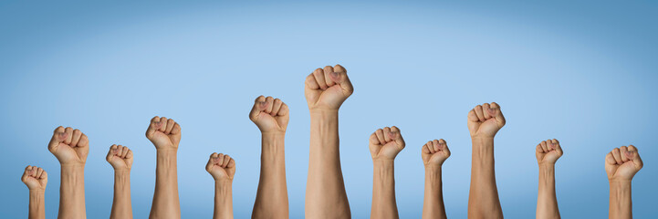 Hands raised up and clenched in a fist on a blue background. Concept of unity of the people, revolution, revolt, riot. Banner