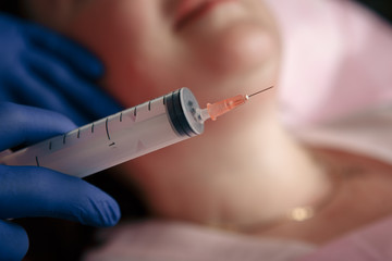 Cosmetologist injecting ozone to chin. Patient is sitting in chair with closed eyes. This therapy is purposed to increase oxygen in a body.