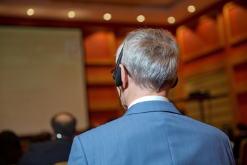 Unrecognizable business people using headphones for translation during event . bald security guard...