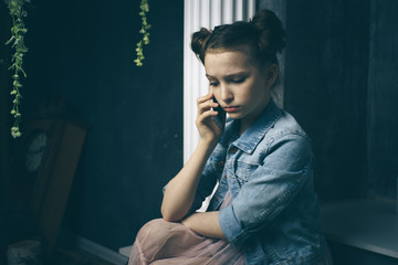Unhappy teen girl looks at her smartphone experiencing anxiety and sad.