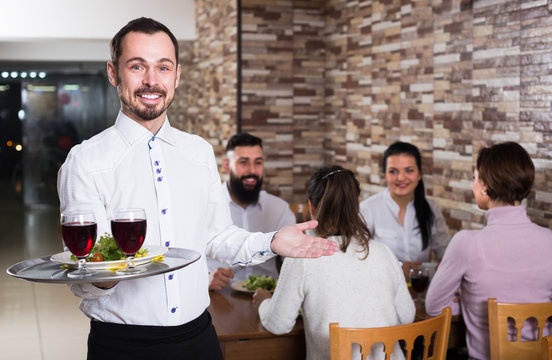 young waiter taking care of adults at cafe table