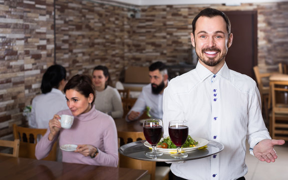 cheerful waiter taking care of adults at cafe table