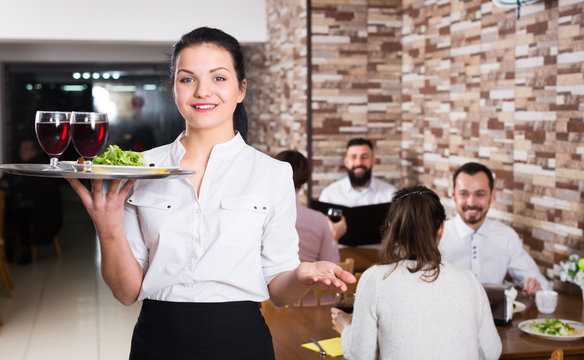 Smiling female waiter greeting customers at table