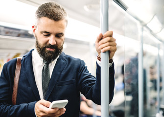 Hipster businessman with smartphone inside the subway in the city, travelling to work.