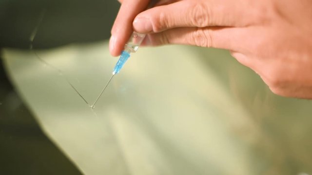 Close-up of a man professionally in the workshop engaged in eliminating cracks on the windshield of the car. Filling the crack with polymer