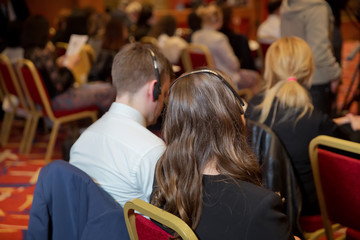 Unrecognizable business people using headphones for translation during event . bald security guard with the headset to control people . heated debate at a conference discussion