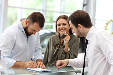 Confident young salesman explaining car features to the young attractive owners