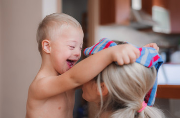 A laughing handicapped down syndrome child with his mother indoors having fun.