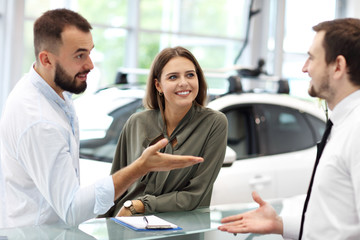 Confident young salesman explaining car features to the young attractive owners