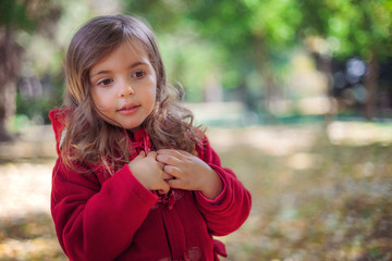 Beautiful little girl sitting in fallen leaves at autumn park