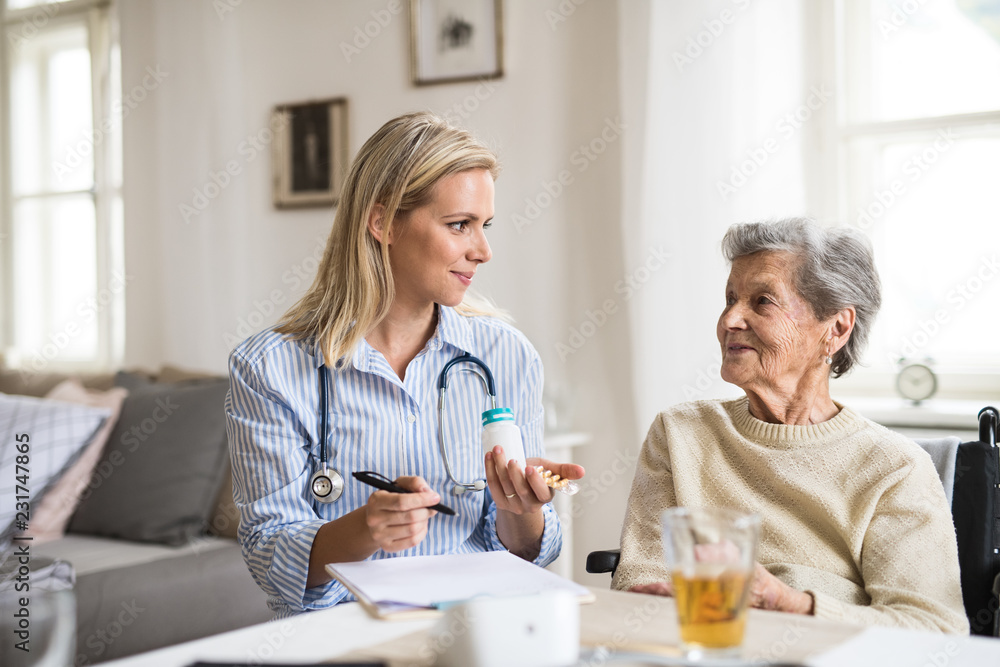 Wall mural A health visitor explaining a senior woman in wheelchair how to take pills.