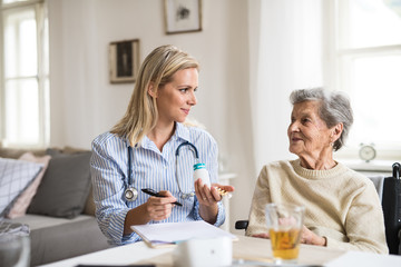 A health visitor explaining a senior woman in wheelchair how to take pills.