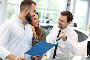 Confident young salesman explaining car features to the young attractive owners