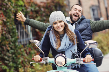 Beautiful young couple smiling while riding scooter in city in autumn