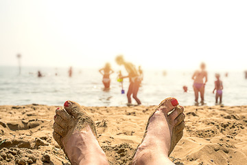 legs of a woman in the sand, nails made up red color, close-up, rest on the beach, silhouettes of people on the seashore background