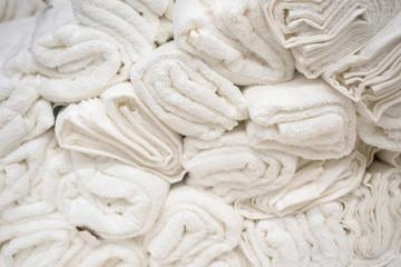 lots of clean, fresh white towels piled on the shelf of a store or in the hotel’s laundry room