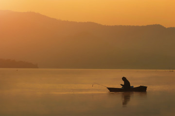 Silhouette Fishing man sitting and look smart phone in his boat with sunset flare effecct and seclective focus, Background for travel or relax, thailand