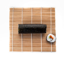 Rollo redondo de sushi con un maki sobre una esterilla visto cenitalmente y sobre un fondo blanco © JesusIgnacio