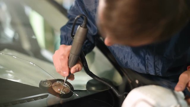 Close-up of a man professionally in the workshop engaged in eliminating cracks on the windshield of the car. Polymer drainage drilling