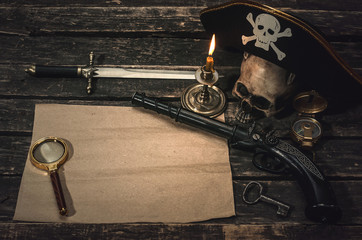 Pirate treasure map with copy space, pirate captain hat, compass, magnifying glass, human skull, musket, dagger and burning candle. Treasure hunter concept background.
