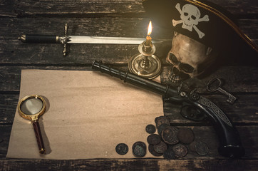 Pirate treasure map with copy space, pirate captain hat, coins, magnifying glass, human skull, musket, dagger and burning candle. Treasure hunter concept background.