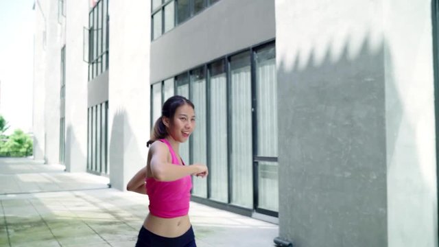 Slow motion - Healthy beautiful young Asian Athlete women sports clothing legs warming and stretching her arms to ready for running on street in urban city. Lifestyle active exercise in city concept.