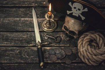 Pirate captain table with pirate hat, human skull, dagger, treasure coins, mooring rope, burning...